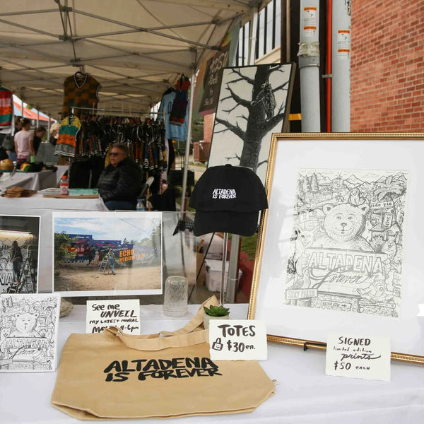 Framed drawings and Altadena tote bags at an artist booth at Webster's anniversary fair