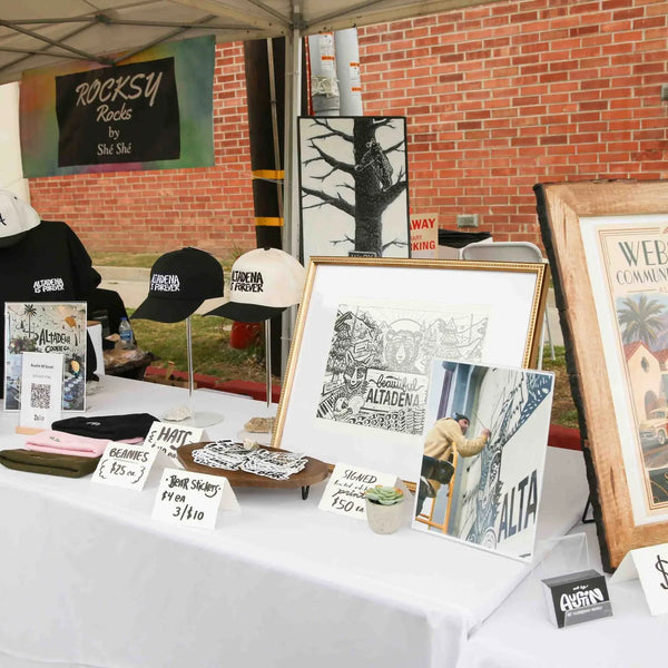 Art prints and caps for sale at a vendor booth during Webster's Pharmacy street fair in Altadena