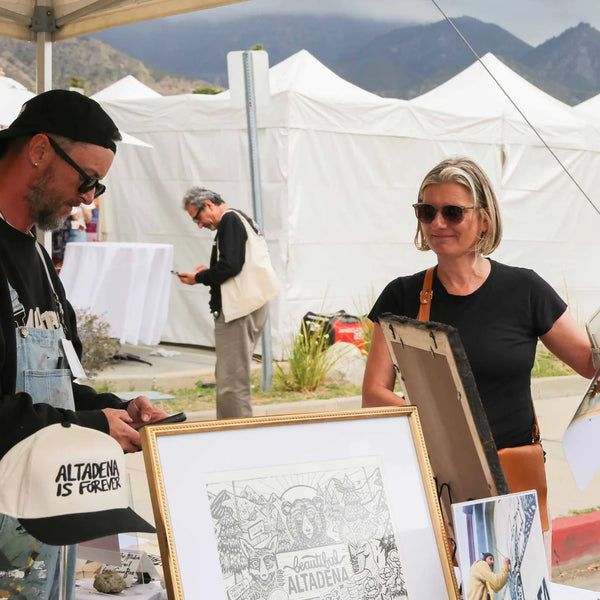 Artist showing a framed Altadena print to a visitor at Webster's street fair