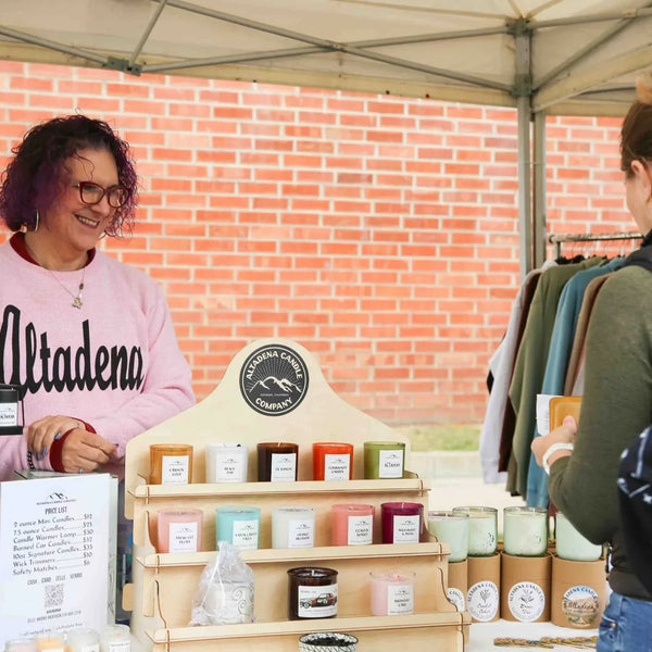 Candle maker in an Altadena sweatshirt helping a customer at Webster's anniversary street fair