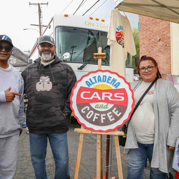 Friends posing with the Altadena Cars and Coffee sign at Webster's fair
