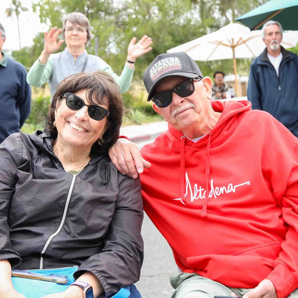 Couple seated with friends waving behind at Webster's anniversary fair