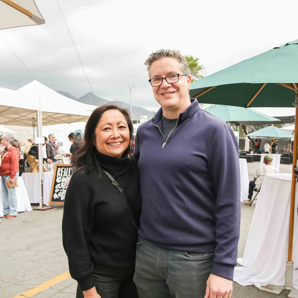 Couple smiling beneath a market umbrella at Webster's anniversary fair