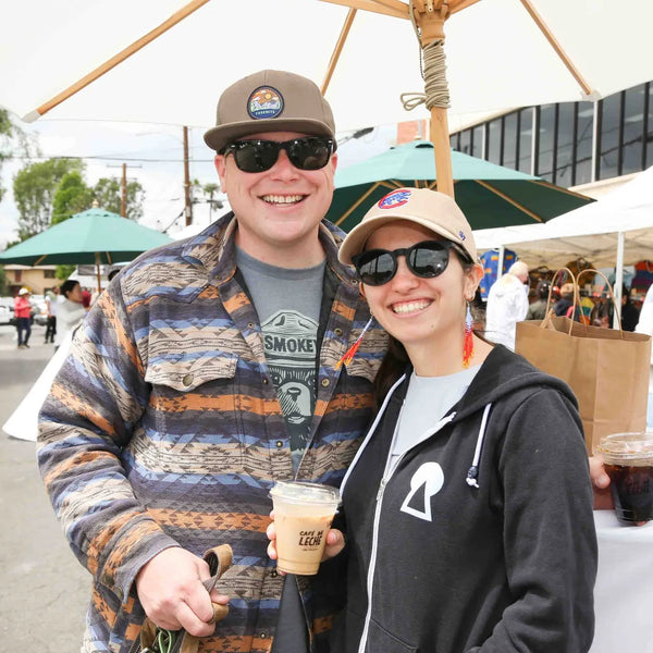 Two friends with iced coffees smiling at Webster's anniversary fair in Altadena