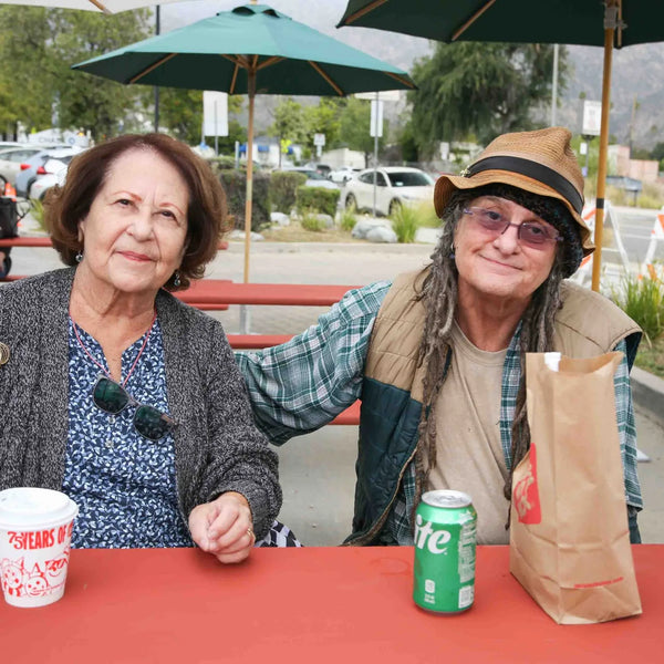 Two friends enjoying coffee at a picnic table during Webster's anniversary street fair