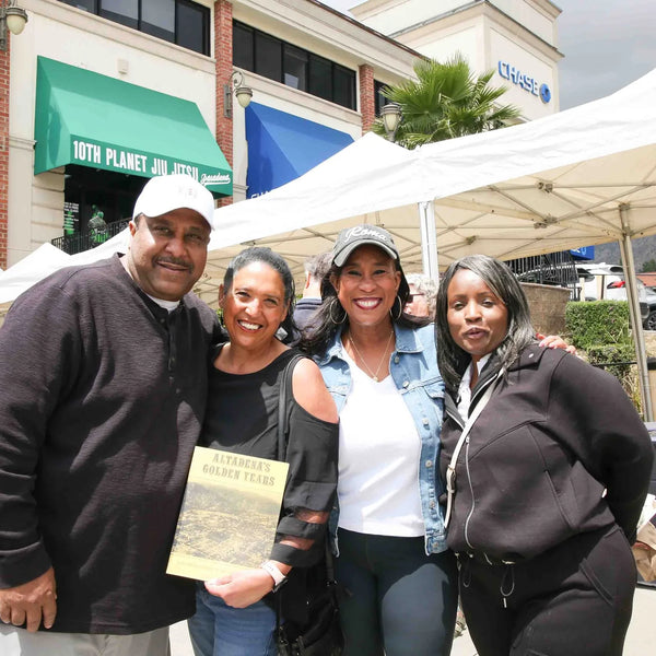 Friends posing with a book at Webster's 100th anniversary street fair