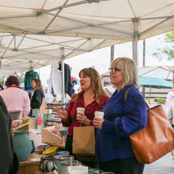 Shoppers with coffee browsing the pottery booth at Webster's street fair