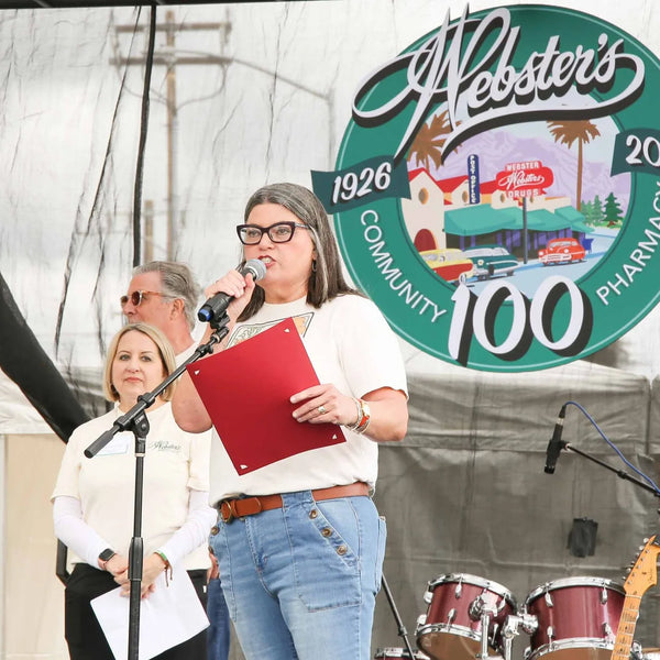 Speaker reading a proclamation beneath the Webster's 1926-2026 centennial logo
