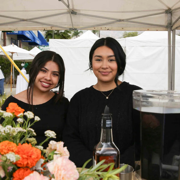 Two volunteers at a flower-decorated refreshment booth at Webster's street fair