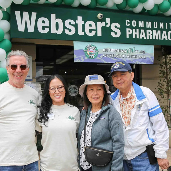 Guests posing under the Webster's Community Pharmacy sign framed by a green and white balloon arch