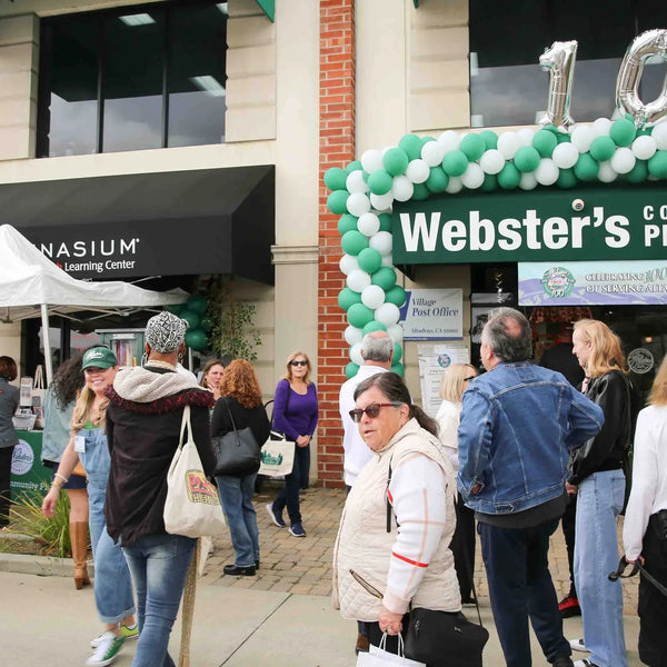 Crowd outside Webster's Community Pharmacy decorated with 100 balloons for the centennial