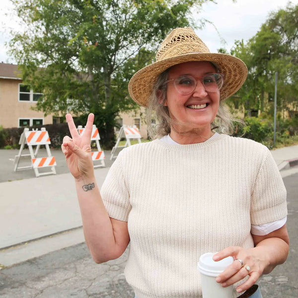 Attendee in a straw hat flashing a peace sign at Webster's street fair in Altadena