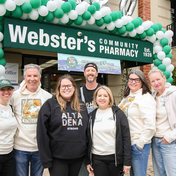 Webster's Pharmacy team beneath the balloon-wrapped storefront sign