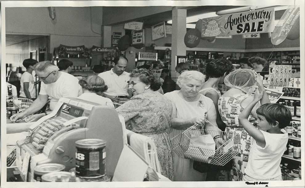 Customers with wire baskets at the Webster’s register during an anniversary sale